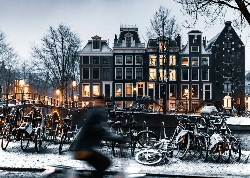 Grachtenpanden met verlichte ramen op een winteravond, met besneeuwde fietsen langs het water