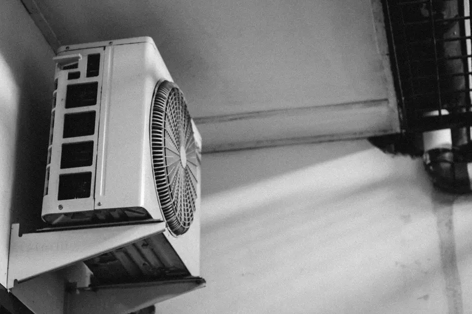 Buitenunit van een airco op een metalen steun aan een gevel, van onderen gezien, in zwart-wit