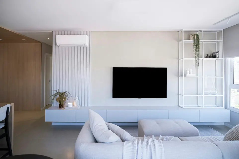 Lichte woonkamer met een witte binnenunit van een split-airco hoog aan de wand, naast een tv-wand en een grote bank
